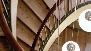 Un escalier en colimaçon avec des marches en bois et une rampe en métal, caractérisé par un design circulaire et des luminaires suspendus.