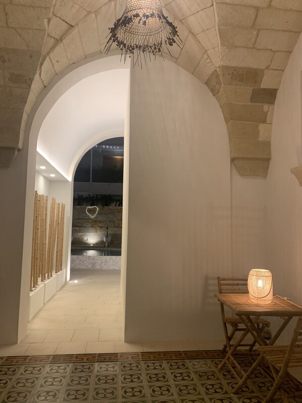 An arched hallway with a patterned floor, a table with a lamp, and a view of a building with a heart-shaped light.