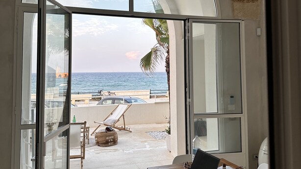 Ein Zimmer mit einem großen Bogenfenster mit Blick auf einen Strand, einem Holztisch mit einem Laptop und einem Stuhl.