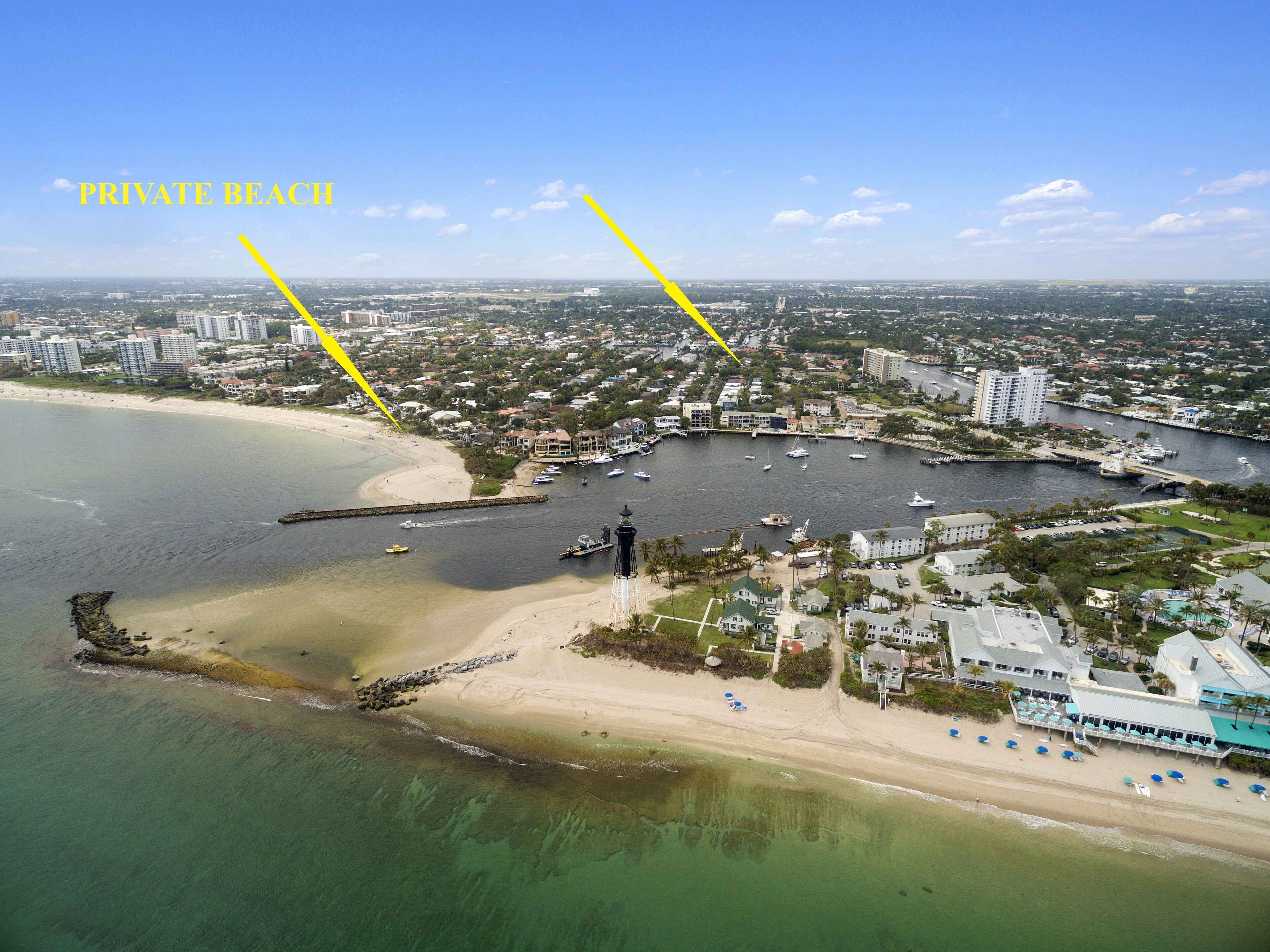 Vue aérienne d’une zone côtière comprenant une plage privée, un port de plaisance et des immeubles résidentiels.