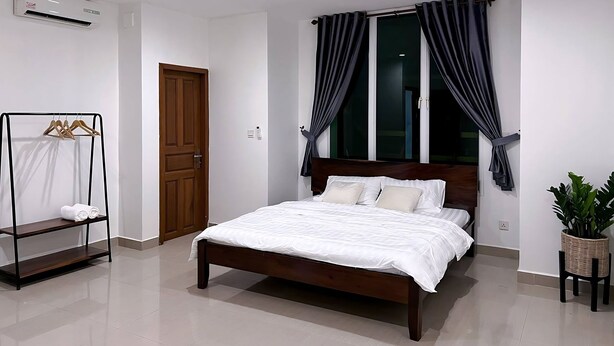 Quarto com cama de madeira, guarda-roupa, janela com cortinas, ar condicionado e um vaso de planta.