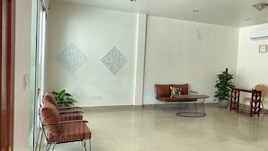 Uma sala ampla com uma mesa redonda e dois sofás, uma grande planta em vaso e decoração na parede.