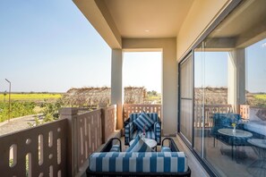 A balcony with a seating area, a glass door, and a view of a green field. - Jay Gurudev Palpur Fort Kuno By Paandora Collections (Karahal)