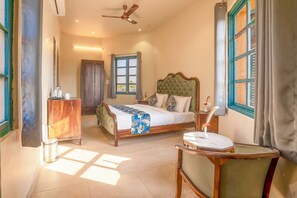 A bedroom with a bed, a desk, a chair, a ceiling fan, and a window with curtains. - Jay Gurudev Palpur Fort Kuno By Paandora Collections (Karahal)
