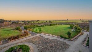 A landscaped outdoor area with a paved walkway, a grassy field, and scattered trees. - Jay Gurudev Palpur Fort Kuno By Paandora Collections (Karahal)