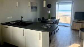 Una cuina moderna amb una illa gran, zona de menjador i un balcó amb vistes a la platja.