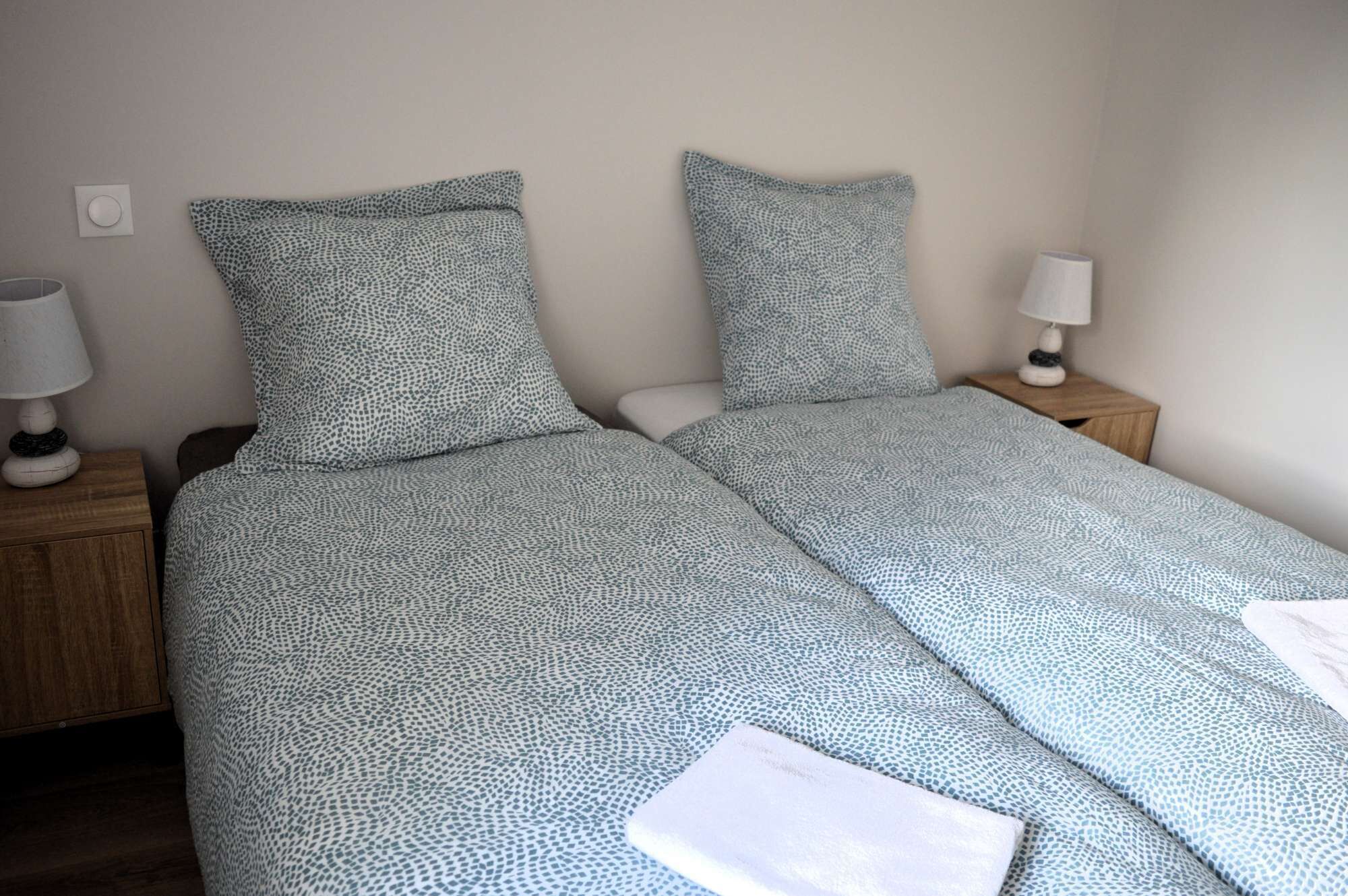 Ein Doppelbett mit gemustertem Überwurf, zwei Kissen, zwei Nachttische mit Lampen und ein Holzbeistelltisch.