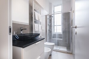 Une salle de bain moderne avec un lavabo noir, des toilettes blanches et une douche à parois de verre.