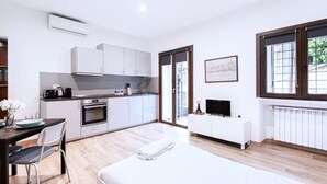 A modern kitchen with white cabinets, a built-in oven, and a dining area with a table and chairs. - Easylife - Studio with balcony in Risorgimento (Milano)