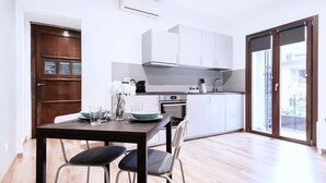 A modern kitchen with white cabinets, a dining table with chairs, and a large window offering a view of the city. - Easylife - Studio with balcony in Risorgimento (Milano)