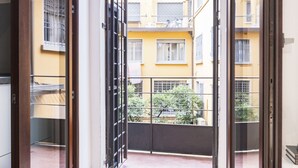 A view through a balcony door with a metal gate, leading to a courtyard with yellow buildings and a bicycle. - Easylife - Studio with balcony in Risorgimento (Milano)