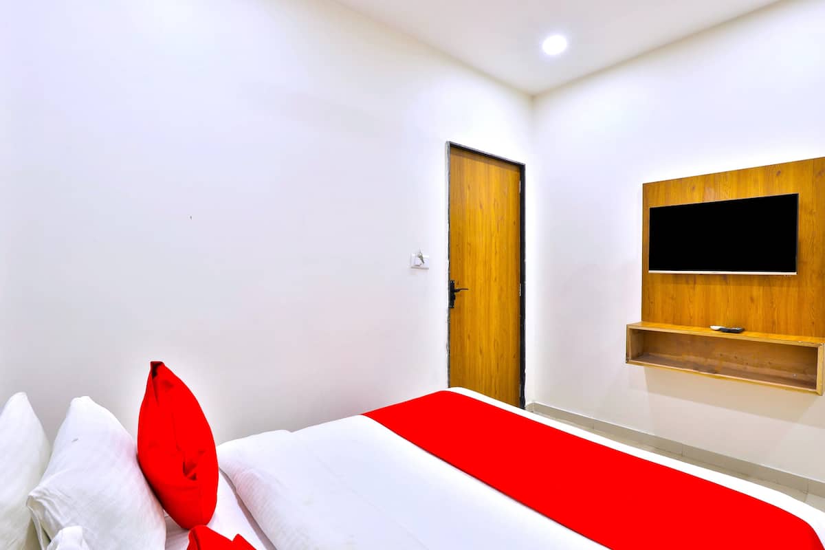 Ein Hotelzimmer mit einem Bett, einer Holztür, einem angebrachten Fernseher und einem roten Detail auf der Bettdecke.