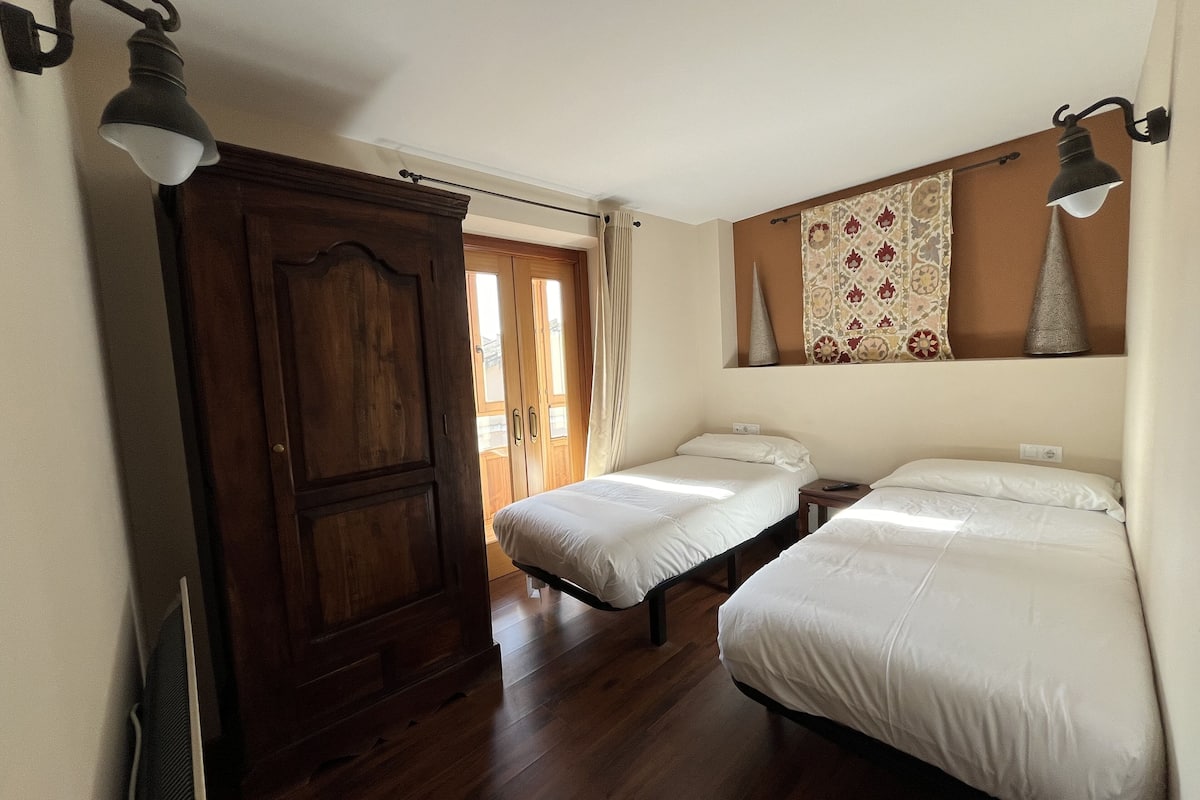 Una habitación con dos camas individuales, un armario de madera y dos lámparas de pared.