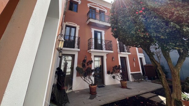 Un edificio de varios pisos con balcones, plantas en macetas y una banca.