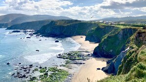 Paisaje costero con acantilados, una playa y cielo despejado.