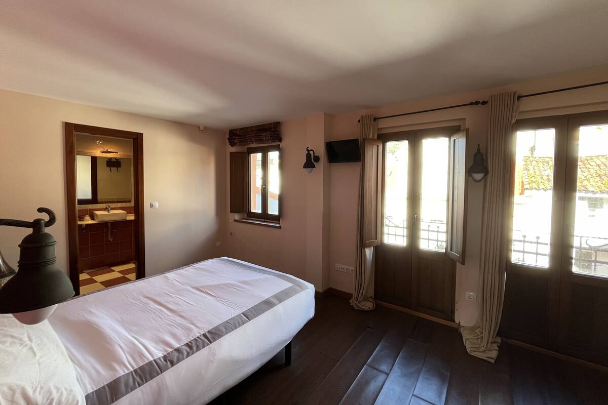 Un dormitorio con cama, ventana, puerta y espejo.