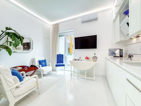 Ein modernes Hotelzimmer mit weißem Design, einem Flachbildfernseher, einem Essbereich und einem großen Fenster.
