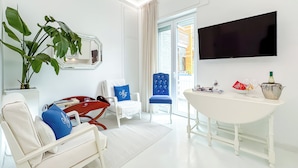 Un salon moderne avec un canapé blanc, un fauteuil bleu, une table à manger, une grande plante en pot et un téléviseur à écran plat.