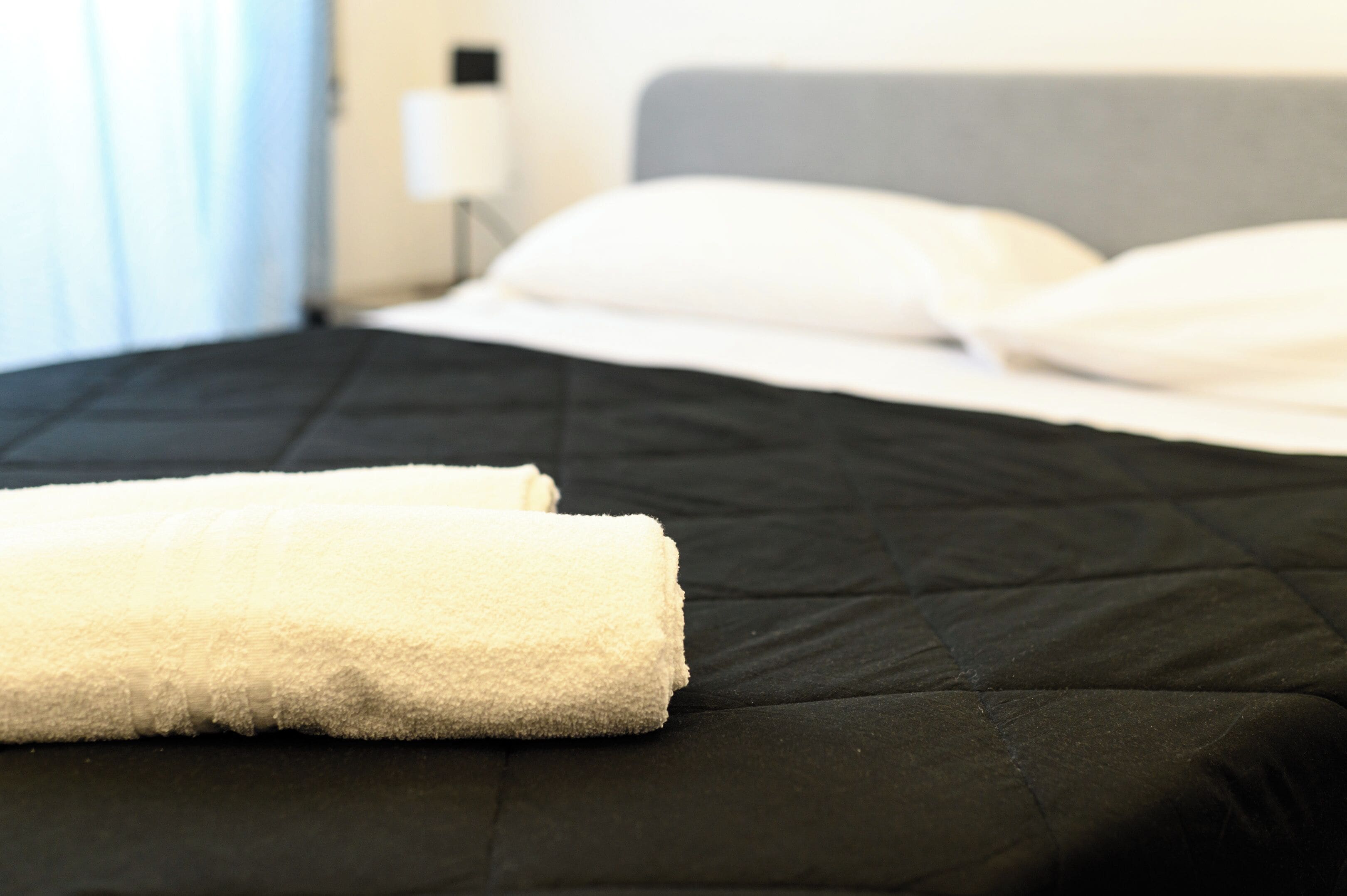 A neatly made bed with white linens and a rolled white towel on a black mattress.