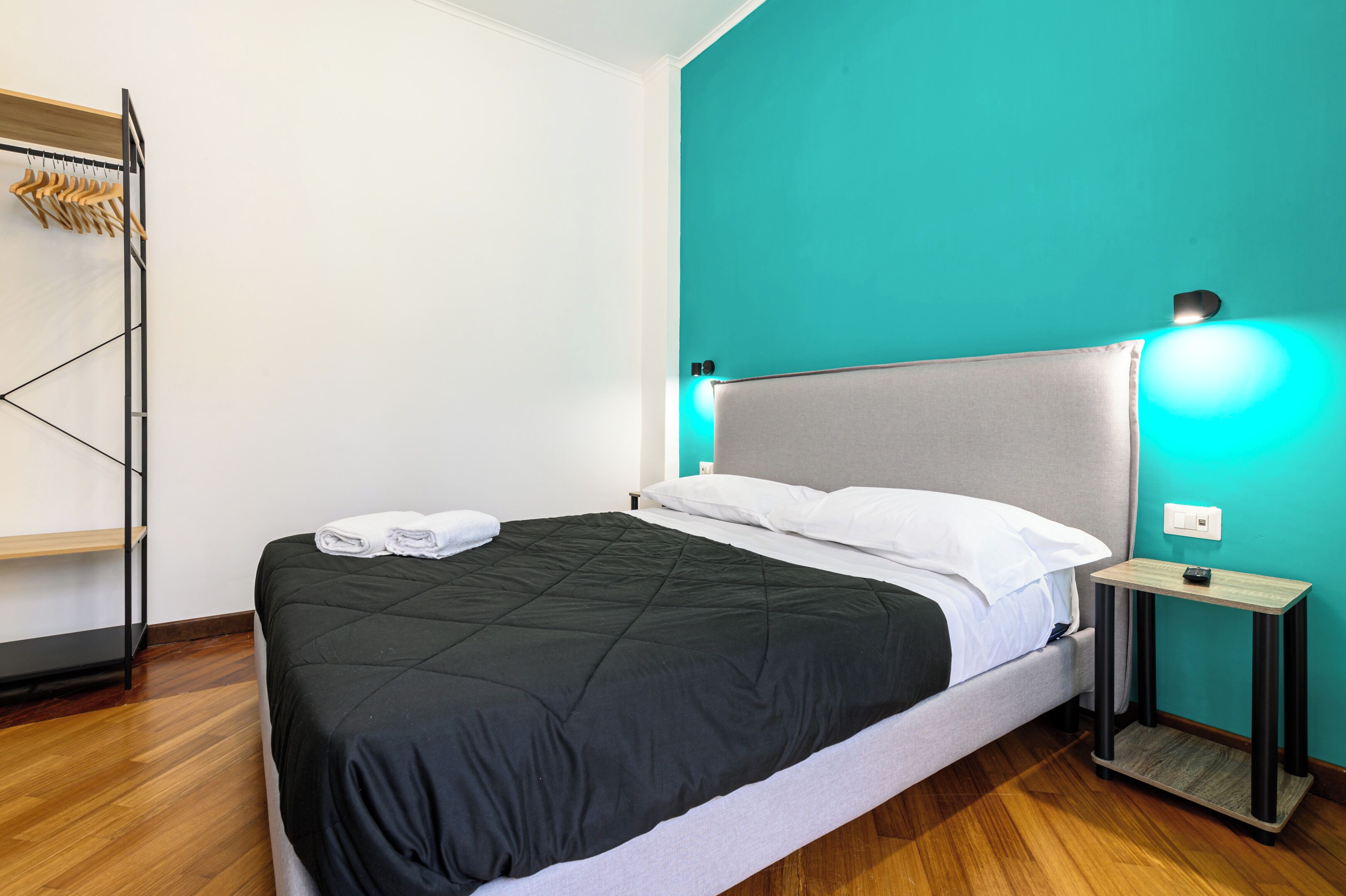 Una cama bien hecha con edredón blanco y negro, una mesita de noche con lámpara y suelo de madera.