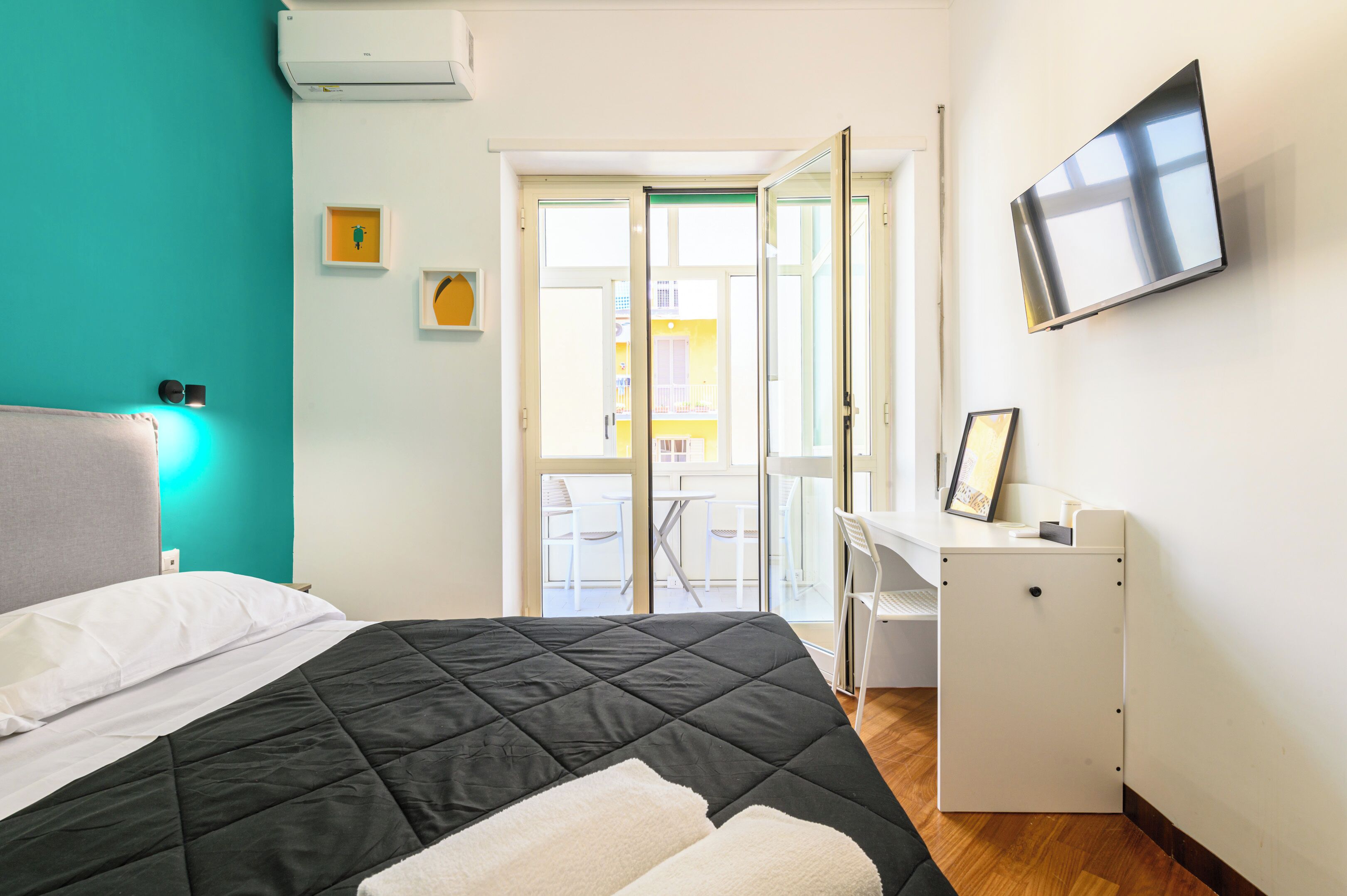 A bedroom with a bed, a desk, a TV, and a sliding glass door leading to an outdoor area.