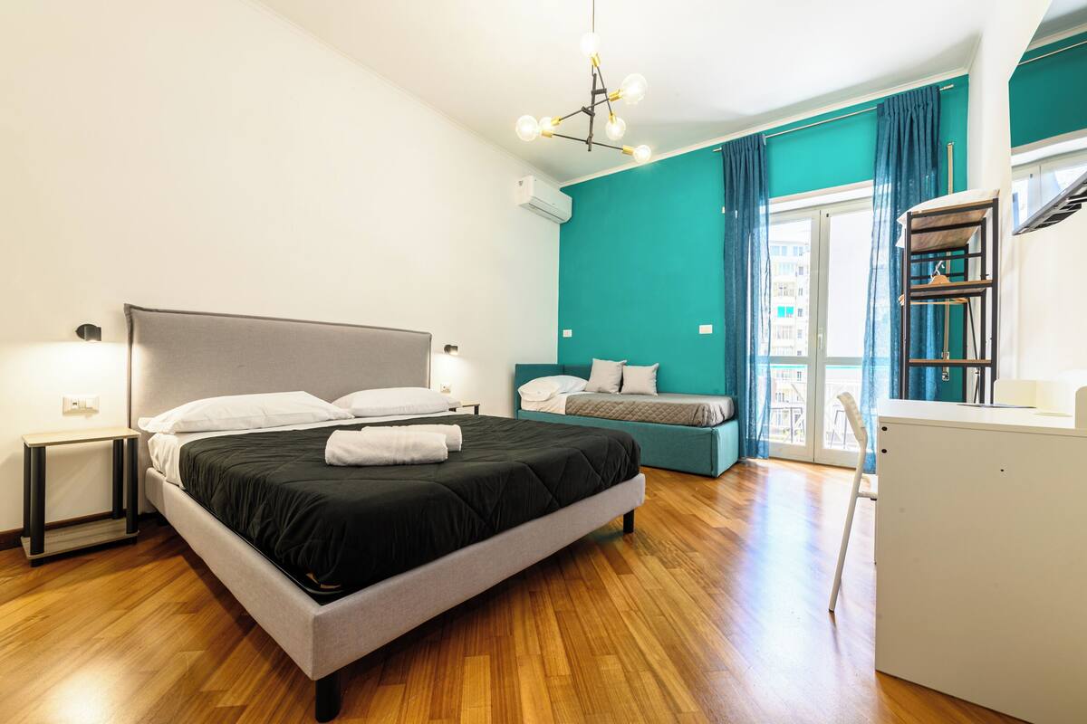 A modern bedroom with a large bed, a bedside table, a desk, and a chair.