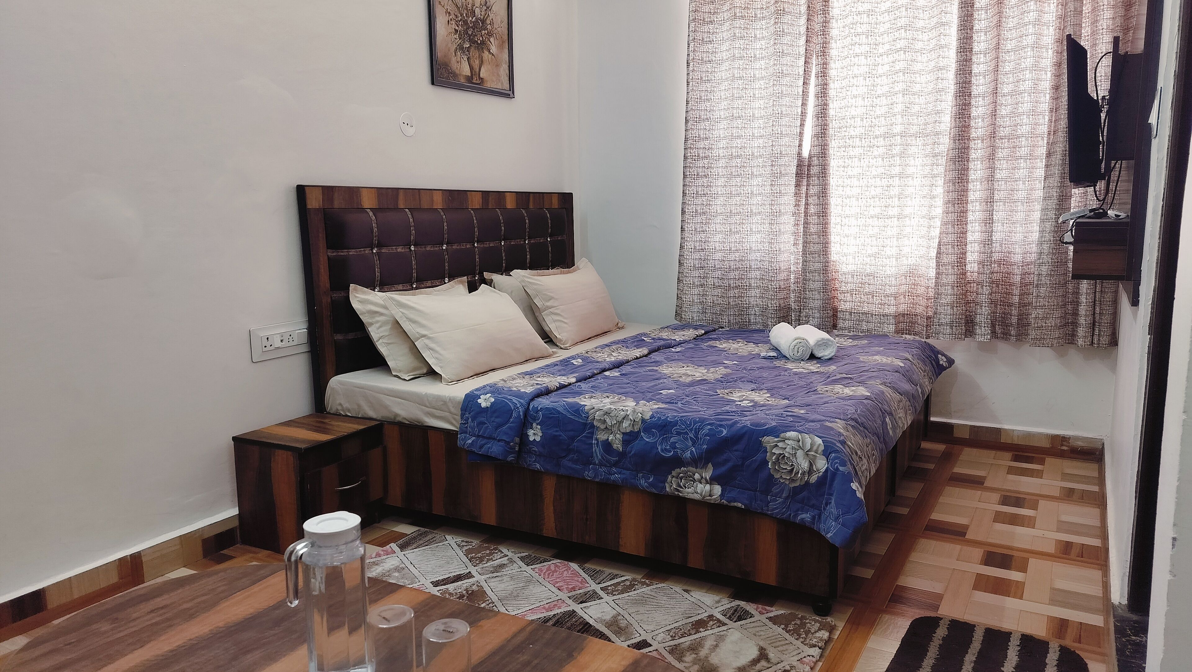 Un dormitorio con cama de madera, mesita de noche, botella de vidrio para agua y alfombra estampada.