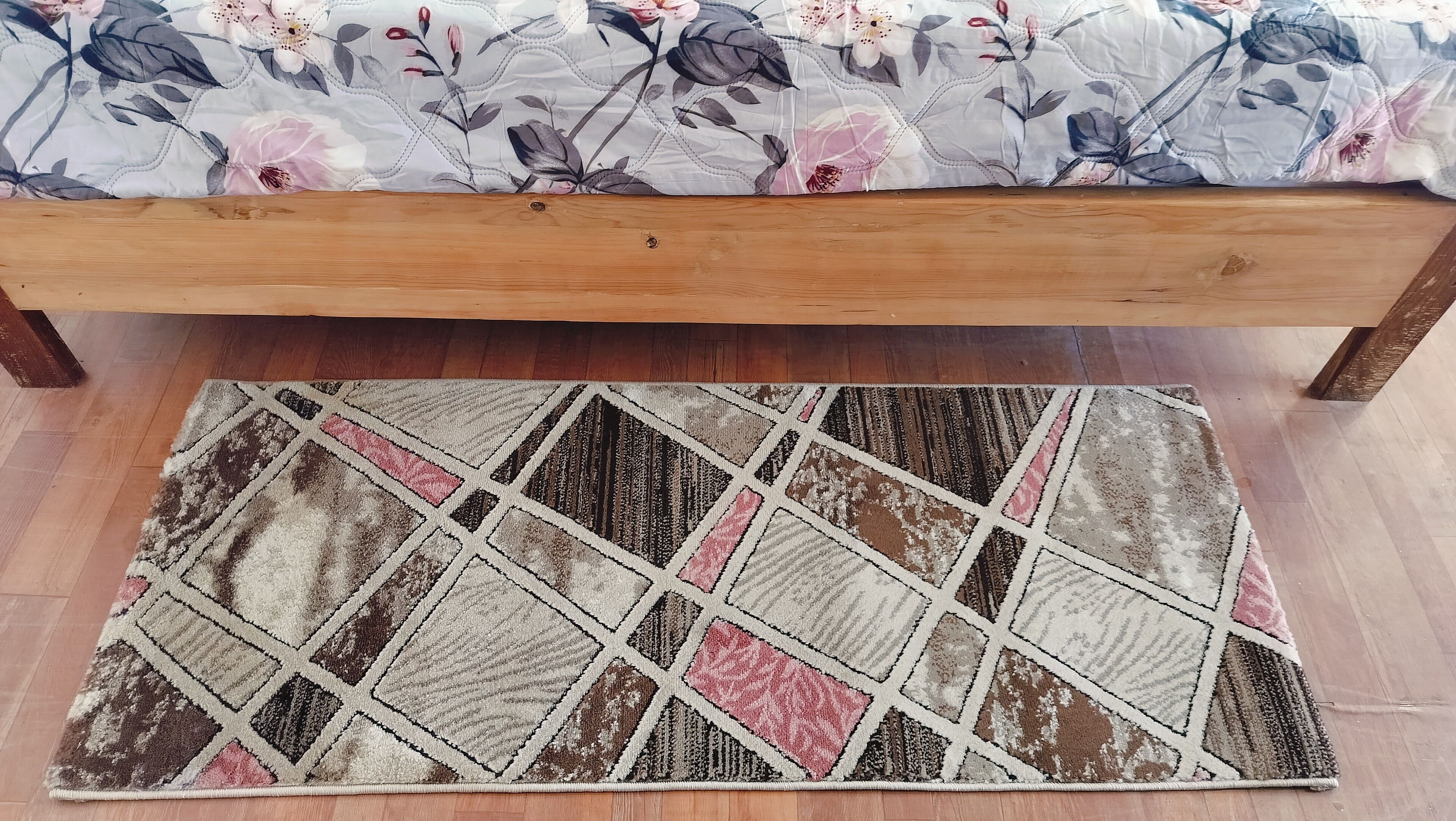 A bed with a floral bedspread and a geometric-patterned rug on a wooden floor.