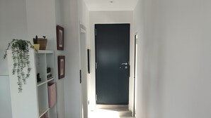 A hallway with a white shelving unit, a dark door at the end, and a light source creating a shadow on the floor. - Relax al pie de la Alfaguara , Ideal Para Escalada, Senderismo y Gastronomía (Fuente Grande)