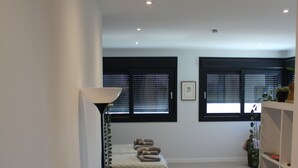 A bedroom with a bed, a floor lamp, a bookshelf, and two windows with blinds. - Relax al pie de la Alfaguara , Ideal Para Escalada, Senderismo y Gastronomía (Fuente Grande)