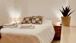 Een net opgemaakt bed met handdoeken, een nachtkastje met een lamp en een plant in een pot.
