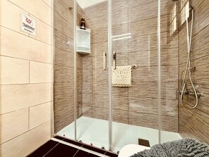 A glass-enclosed shower stall with a towel rack and a bottle on a shelf.