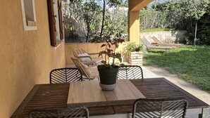 Un patio techado con mesa de madera y cuatro sillas, rodeado de follaje y vistas a árboles.