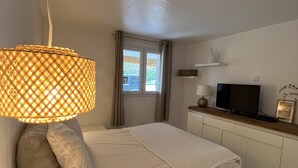 Un dormitorio con cama, televisión, lámpara y ventana con cortinas.