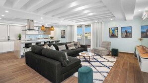 A modern living room with a dark sofa, a coffee table, and a view of the kitchen. - Beach Condo by Otium | Steps from Oceanpark Beach (San Juan)