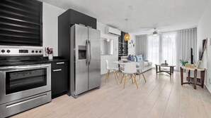 A modern kitchen with a built-in oven and refrigerator, a dining area with a white table and chairs, and a living space with a sofa and a coffee table. - Beach Condo by Otium | Steps from Oceanpark Beach (San Juan)