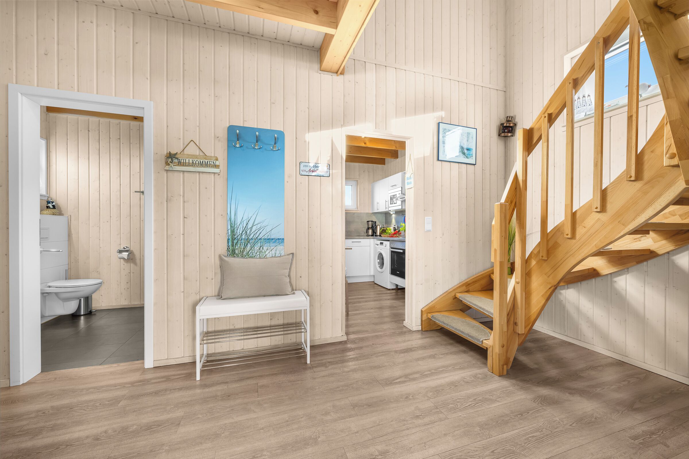A wooden interior with a staircase, a bench, a welcome sign, and a view of the kitchen.