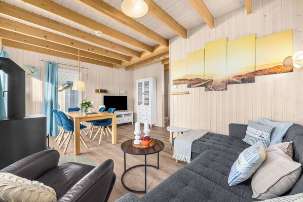 Una sala de estar moderna con un sofá, un comedor con mesa y sillas, y una zona de cocina con refrigerador y armarios.