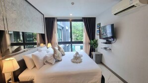 Une chambre d’hôtel avec un grand lit, un téléviseur à écran plat, une fenêtre avec des rideaux et un appareil de climatisation.