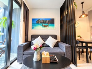 Un salon moderne avec un canapé gris, une table basse ronde et un tableau représentant un bateau sur une plage.