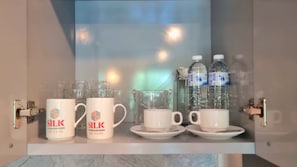 Eine Minibar mit zwei Kaffeetassen der Marke SILK, zwei weißen Tassen, einer Glaskaraffe und drei Wasserflaschen.