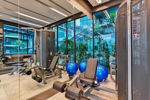 A modern gym with exercise equipment, large windows, and a view of a building with stairs and greenery. - B406 - 1 Bedroom Serviced Apartment Pool View Near Ao Nang Beach (Tambon Ao Nang)