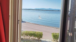 A view from a window overlooking a calm body of water with a distant shoreline and mountains.
