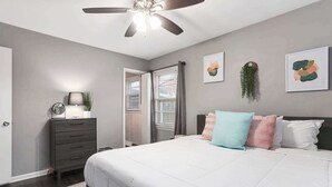 Une chambre à coucher comprenant un lit, une commode, un ventilateur de plafond et des œuvres d’art accrochées aux murs.