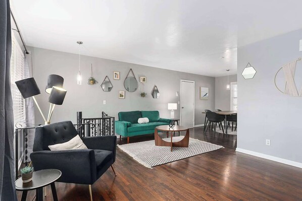 A modern living room with a black armchair, a green sofa, and a dining area with a table and chairs.
