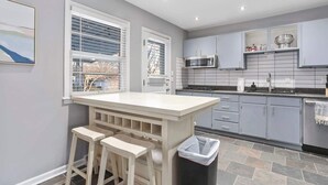 Une cuisine moderne avec des meubles gris, un plan de travail blanc et un petit coin bar avec des tabourets.