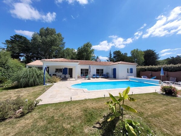 Une maison avec une piscine, un patio couvert et un jardin.