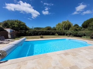 Une piscine rectangulaire, bordée d’une terrasse carrelée, entourée d’une pelouse et d’arbres.