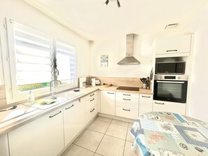 Una cocina con gabinetes blancos, una campana extractora de acero inoxidable, un microondas y un horno.