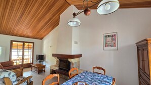A dining area with a table set for four, a fireplace, wooden ceiling, and a television in the background.